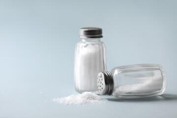 Two salt shakers full of table salt in front of a neutral background